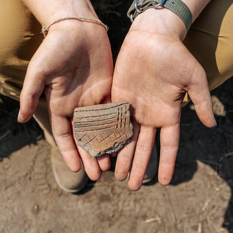 Boyd Archaeological Field School student displays artifact unearthed at dig site