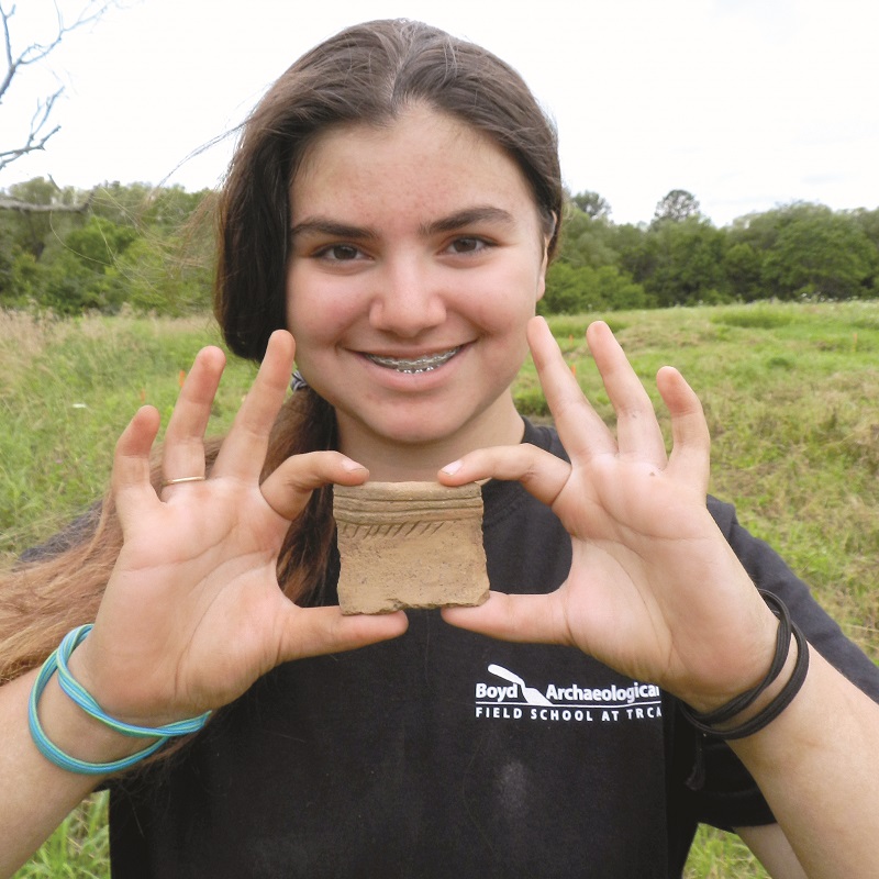 Boyd Archaeological Field School student displays artifact unearthed at dig site